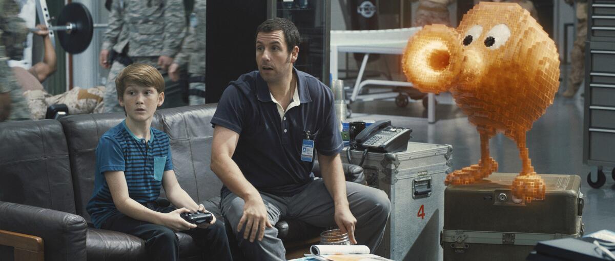 Matthew Lintz, izquierda, en el papel de Matt, y Adam Sandler como Sam Brenner con Q*bert en la película "Pixels" de Columbia Pictures. La película se estrena en Estados Unidos el 24 de julio de 2015. (Sony Pictures via AP)