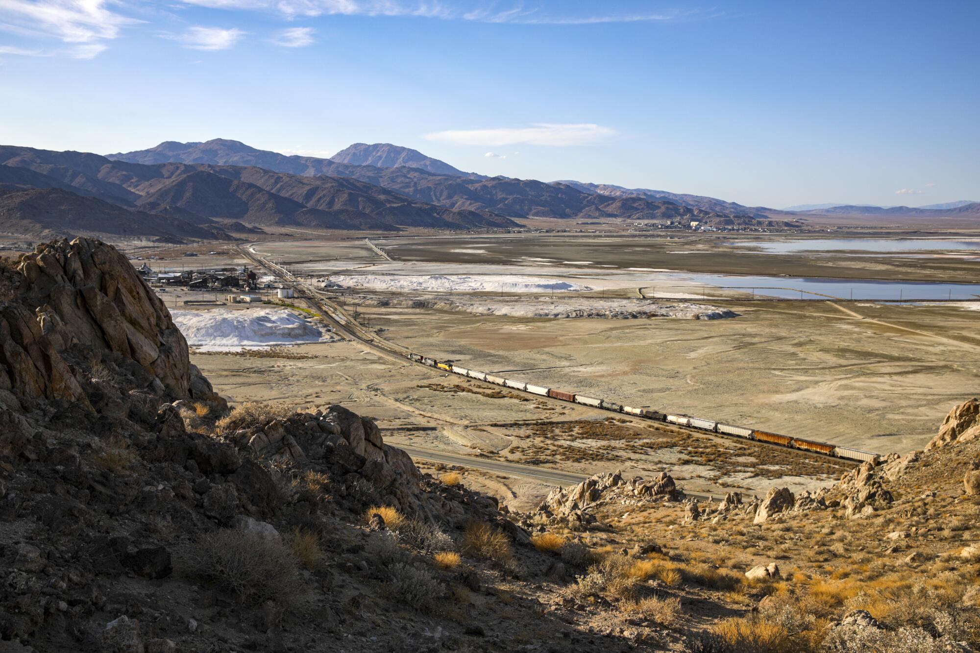 A freight train in a desert valley, viewed from a hillside