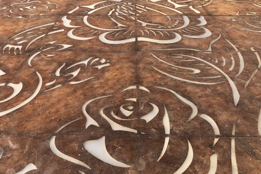 A detail view of Corten steel plate laying on the ground show outlines of roses and a pair of praying hands