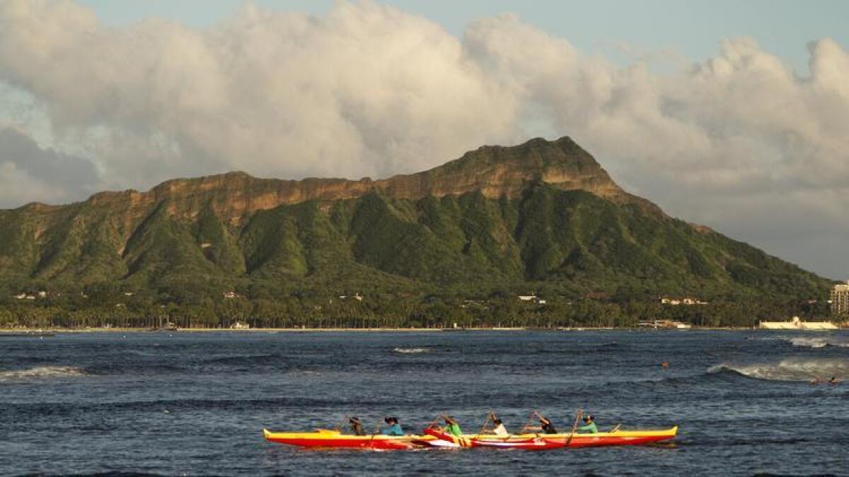 Una canoa con portaremos exteriores pasando más allá de la montaña de Diamond Head en Honolulu. Hawái es un destino popular para los legisladores de California cada mes de noviembre, aunque prefieren Maui.
