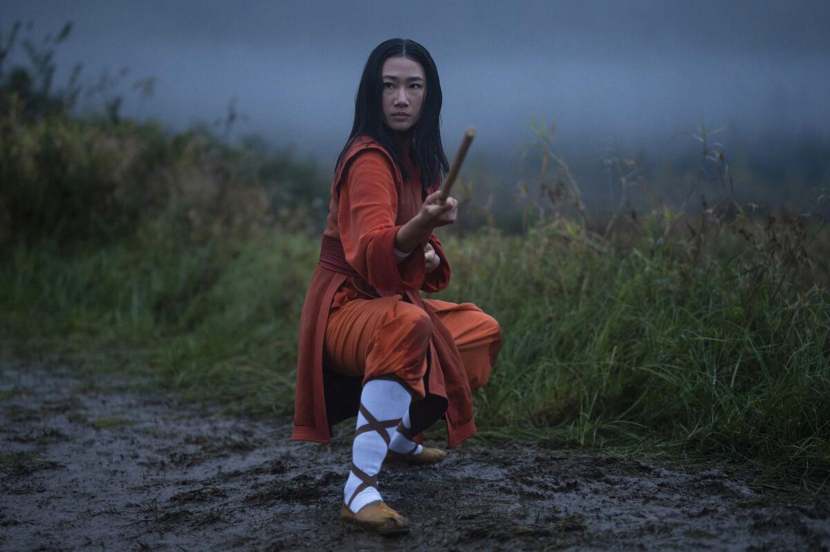 A woman practices kung fu in the fog on a muddy path. 