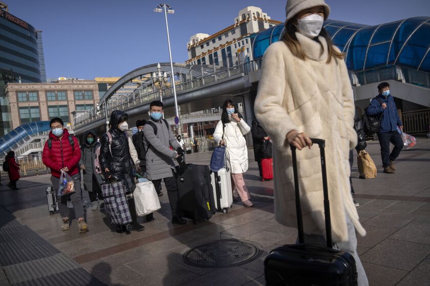 Travelers wearing face masks walk toward the entrance of the Beijing Railway Station in Beijing, Saturday, Jan. 14, 2023. Millions of Chinese are expected to travel during the Lunar New Year holiday period this year. (AP Photo/Mark Schiefelbein)