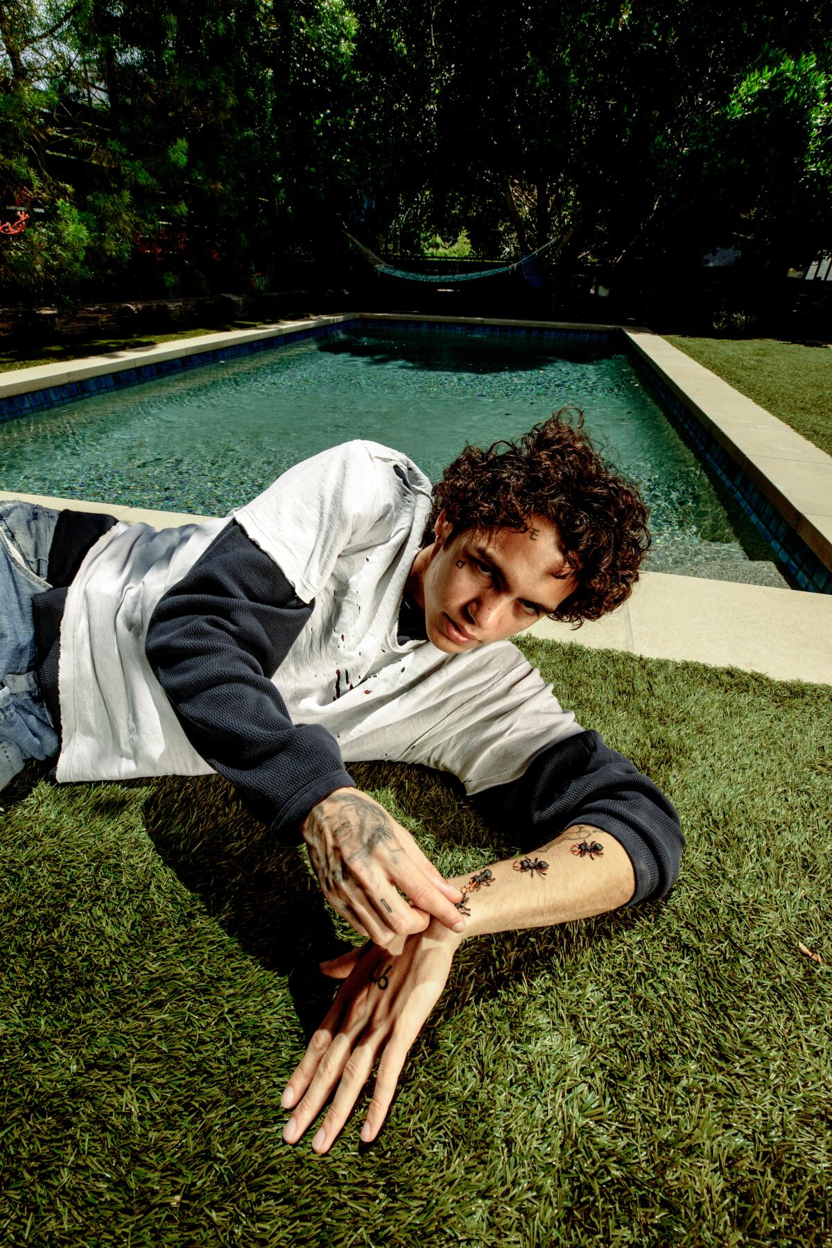 Dominic Fike reclines on the grass next to a rectangular pool