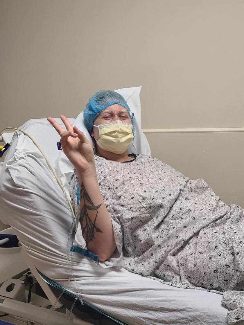 A woman in a hospital gown poses for a photo before a surgery.