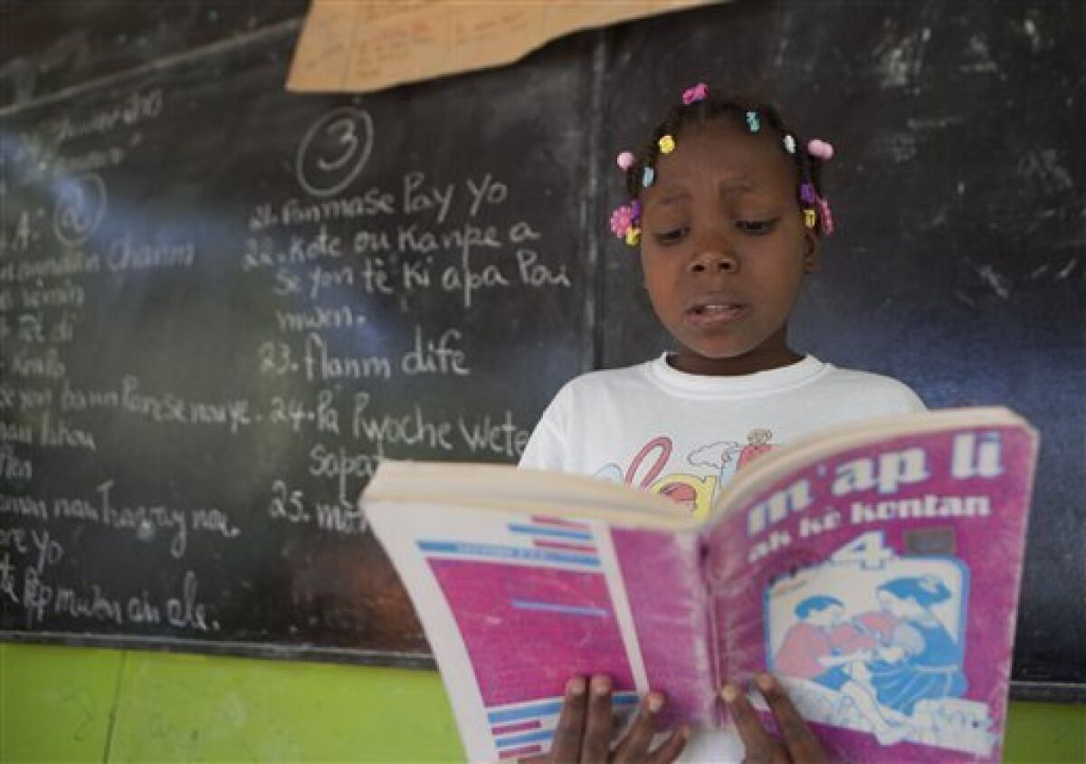 In this Jan. 24, 2013 photo, Cassandra Meon, 11, reads a textbook before her classmates that reads in Creole "I'm Reading With a Happy Heart" as she attends her Creole language class at the Louverture Cleary School, which also teaches French, English and Spanish, in Croix-des-Bouquets, Haiti. Creole advocates say that there’s no shortage of Creole-language books and point to publishing houses such as Educa Vision, Inc. in Florida, which produce such materials. But they acknowledge that shipping the materials to Haiti is expensive and goods are often held up in customs. (AP Photo/Dieu Nalio Chery)