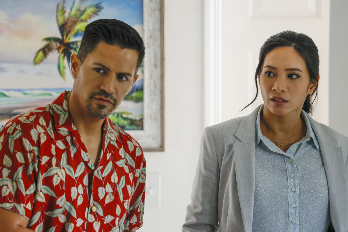 A man in a Hawaiian shirt and a woman in a gray blazer look to the left.