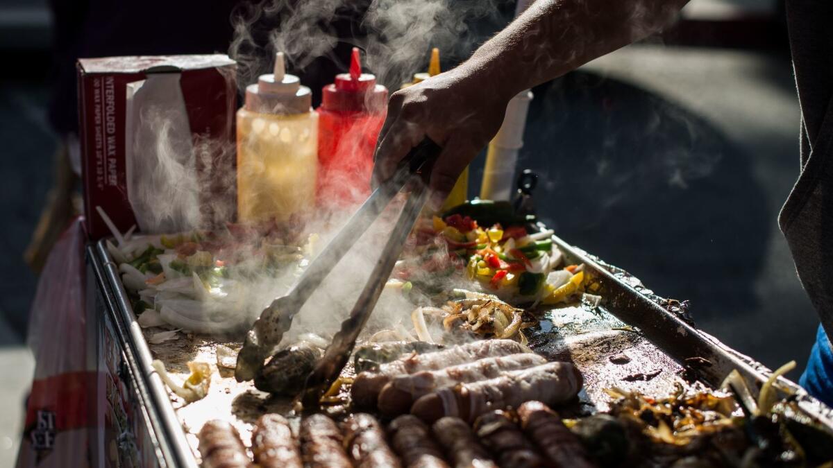 A street vendor prepares hot dogs on a sidewalk in downtown Los Angeles in March. The Costa Mesa City Council decided Tuesday to hold off on voting on a new sidewalk vending ordinance until the city comes up with a more flexible version that would "open up opportunities for more businesses."