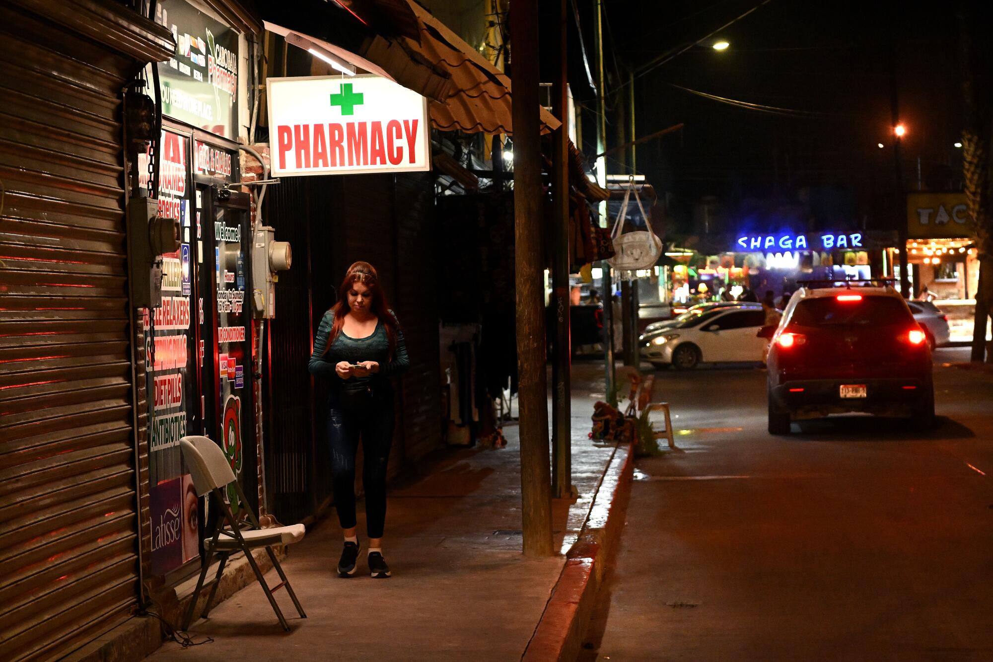 A person walks under a "Pharmacy" sign on a sidewalk.