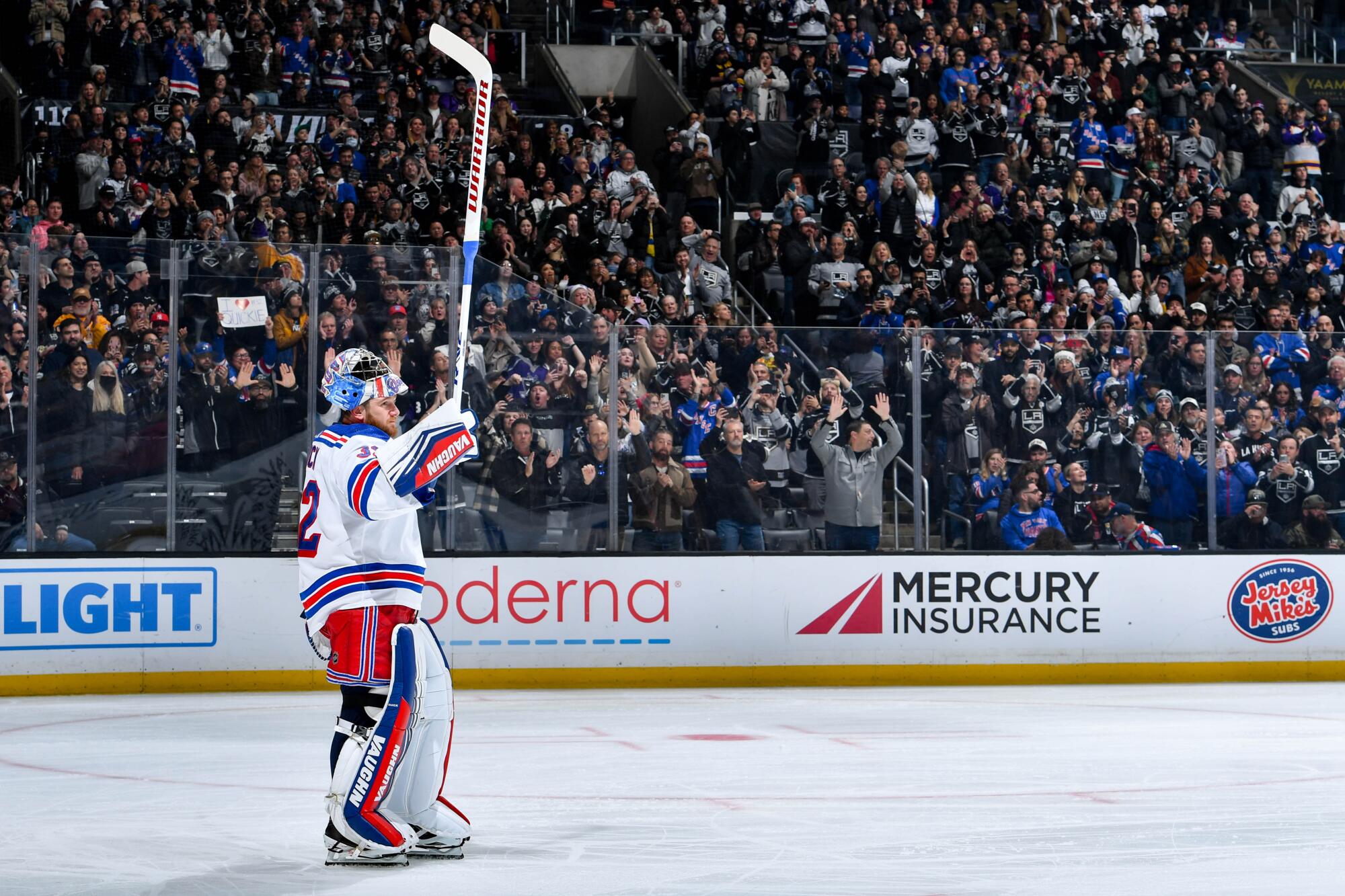 New York Rangers goalie Jonathan Quick raises his hockey stick at the crowd after being applauded.