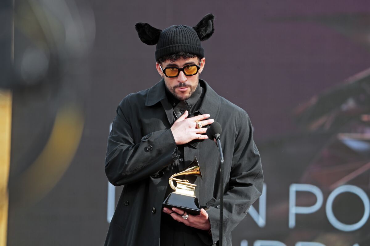 A man places his hand over his heart while standing in front of a microphone and holding a Grammy trophy