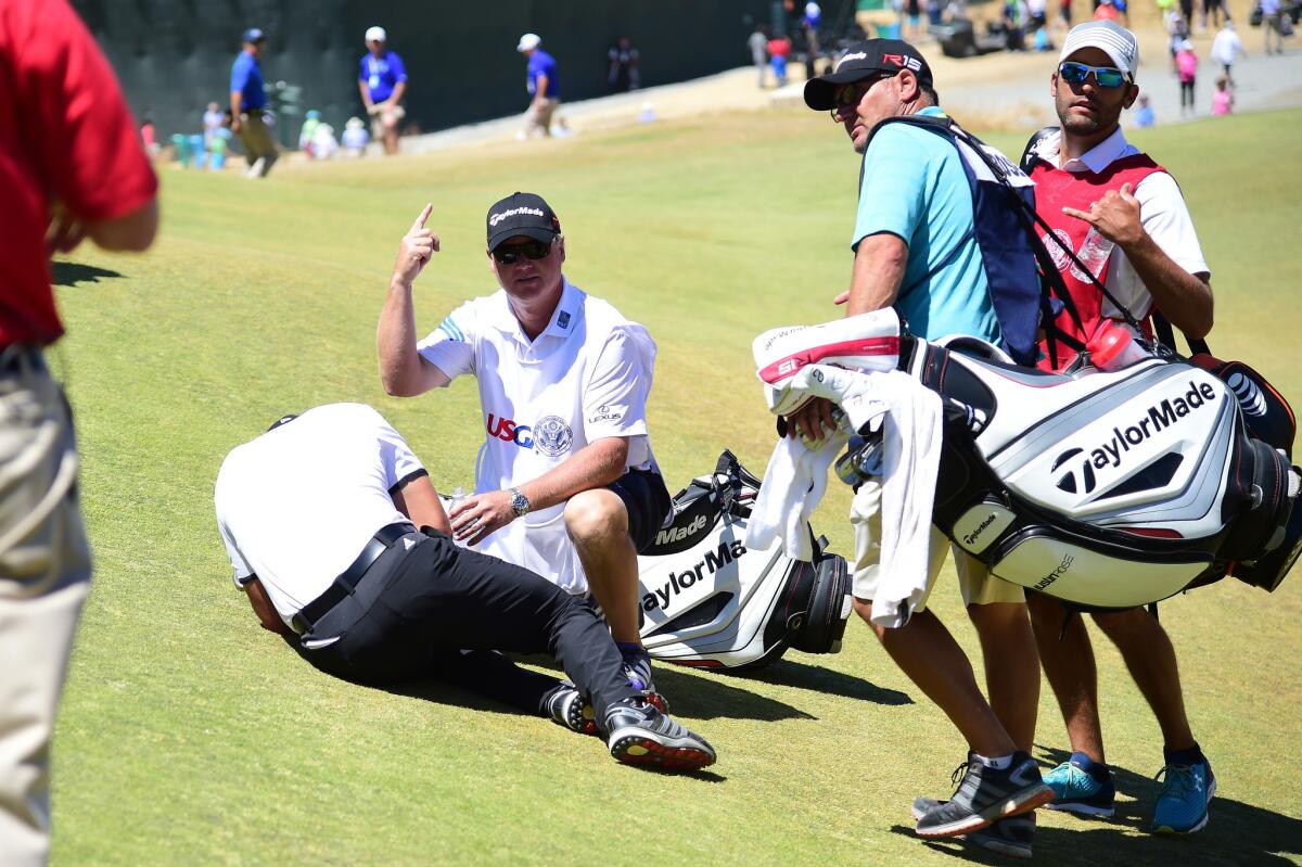 Jason Day is tended to by caddie Colin Swatton as he lays on the ninth green after collapsing because of dizziness during the second round of the 115th U.S. Open at Chambers Bay in University Place, Wash.