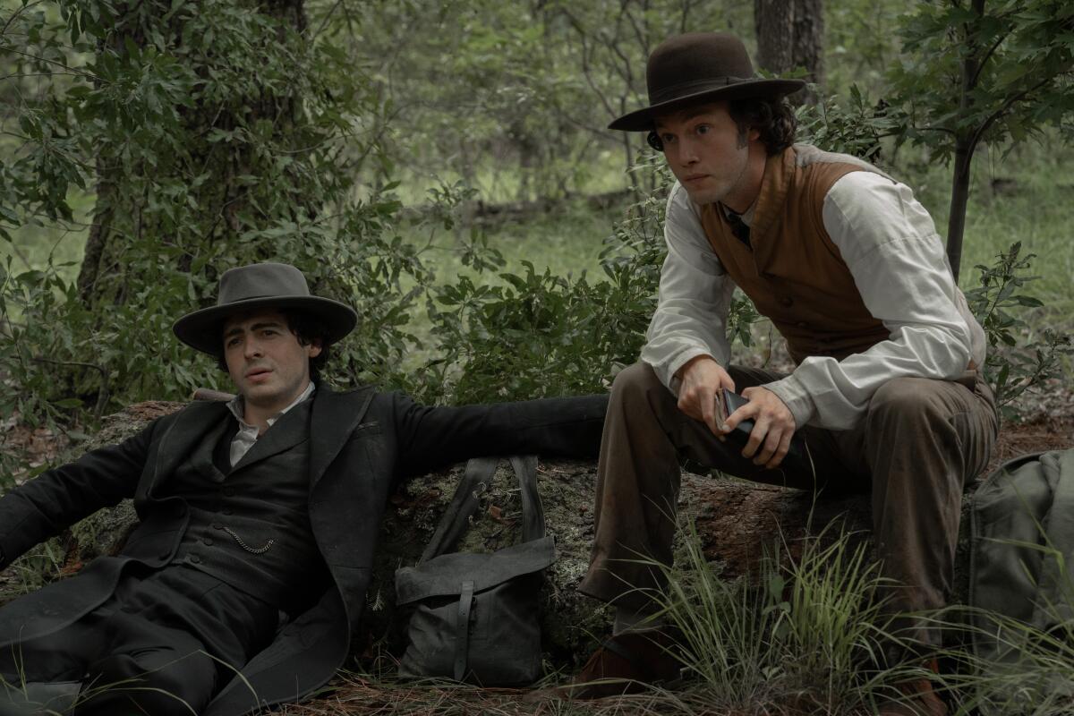 Two men in period costume sitting in the woods.