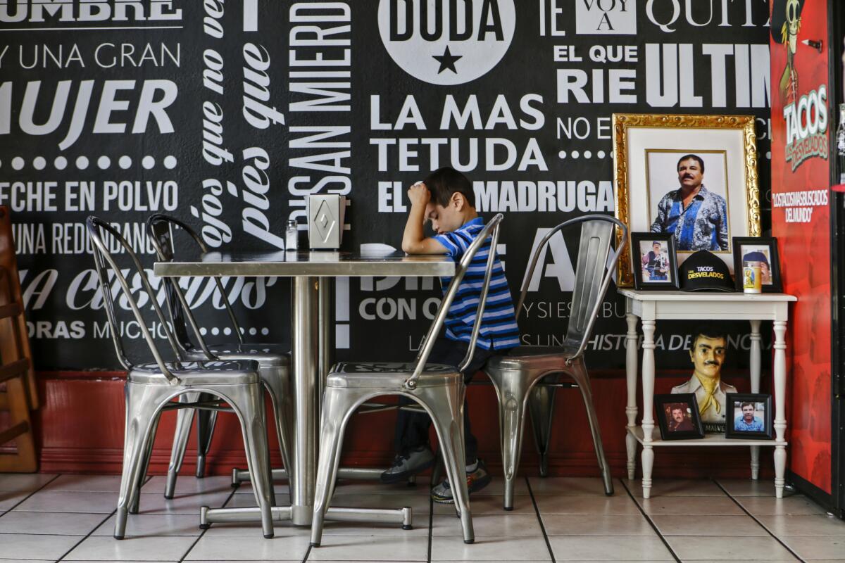 Fabricio Ramirez Jr., son of the owner of Tacos Los Desvelados, sits at a table inside the drug lord-themed taqueria in Maywood.