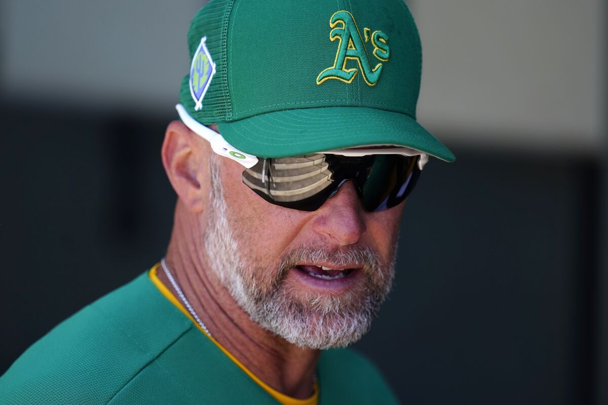 Oakland Athletics manager Mark Kotsay talks with coaches in the dugout prior to the team's spring training baseball game against the Colorado Rockies on Saturday, April 2, 2022, in Mesa, Ariz. (AP Photo/Ross D. Franklin)