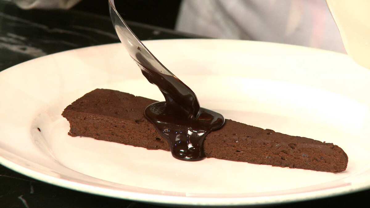 Chef Nancy Silverton spoons warm chocolate onto a slice of chocolate cake. Cake recipe.