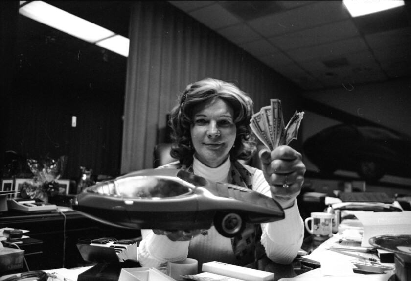 Elizabeth Carmichael holding a model of the Dale and fistful of cash