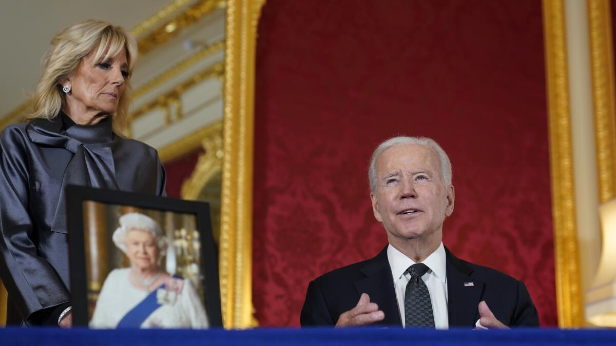 President Biden signs a book of condolence as first lady Jill Biden looks on.