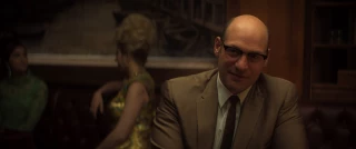 Soprano Junior, interpretado por un Corey Stoll con gafas, se sienta en una mesa en 