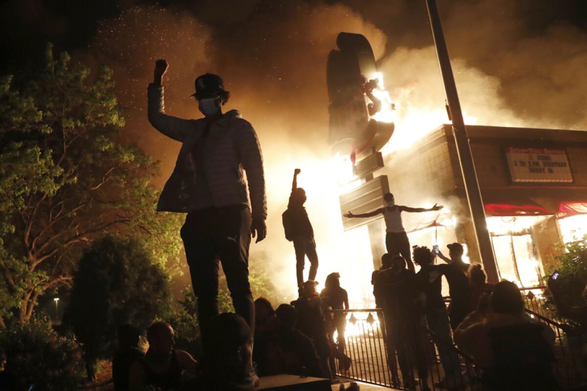 A protester stands, fist raised, in front of a burning fast food restaurant in Minneapolis.