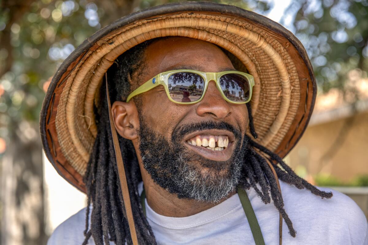 A smiling man wears sunglasses and a woven straw hat.