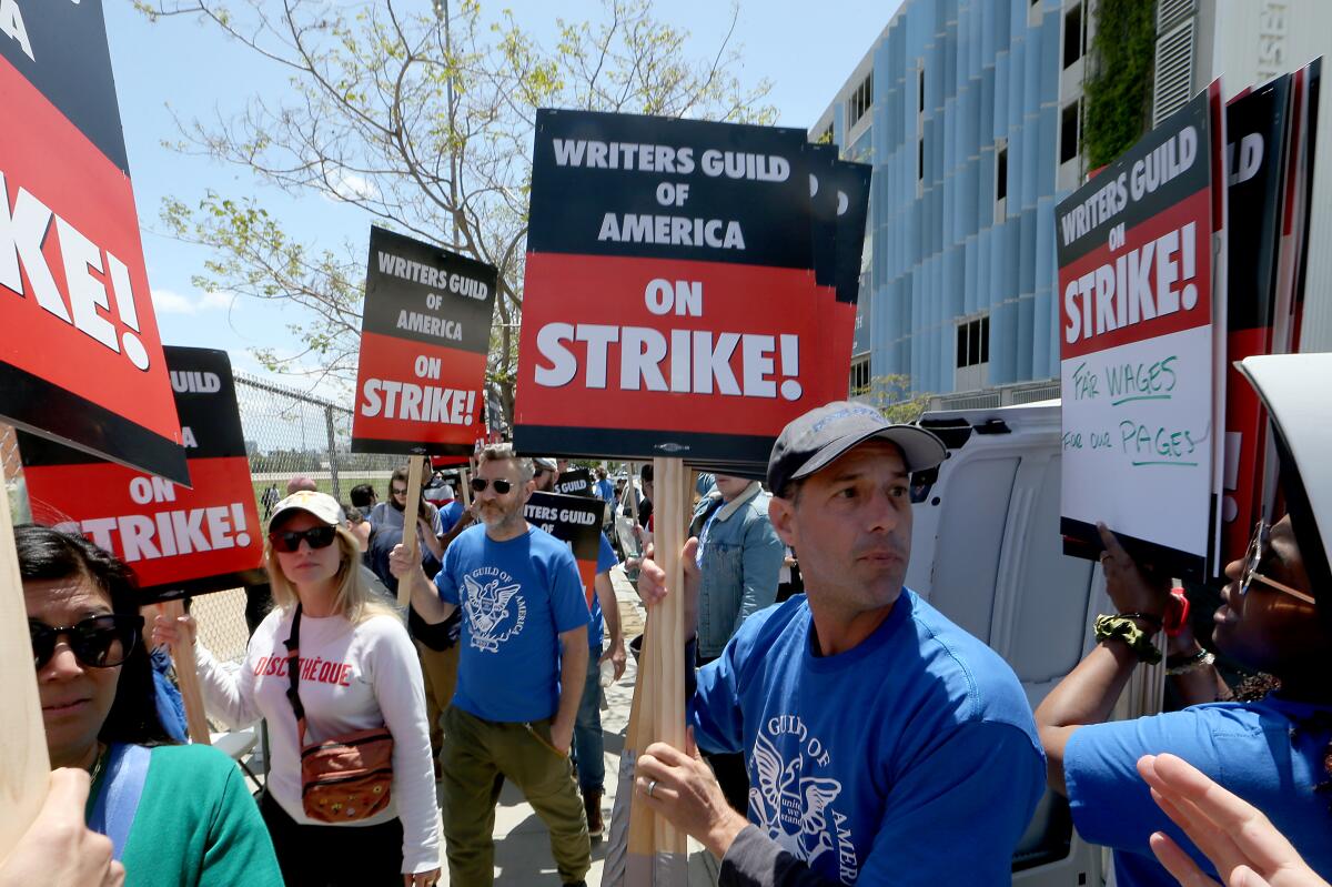 Strikers hold signs as they picket outside a building.