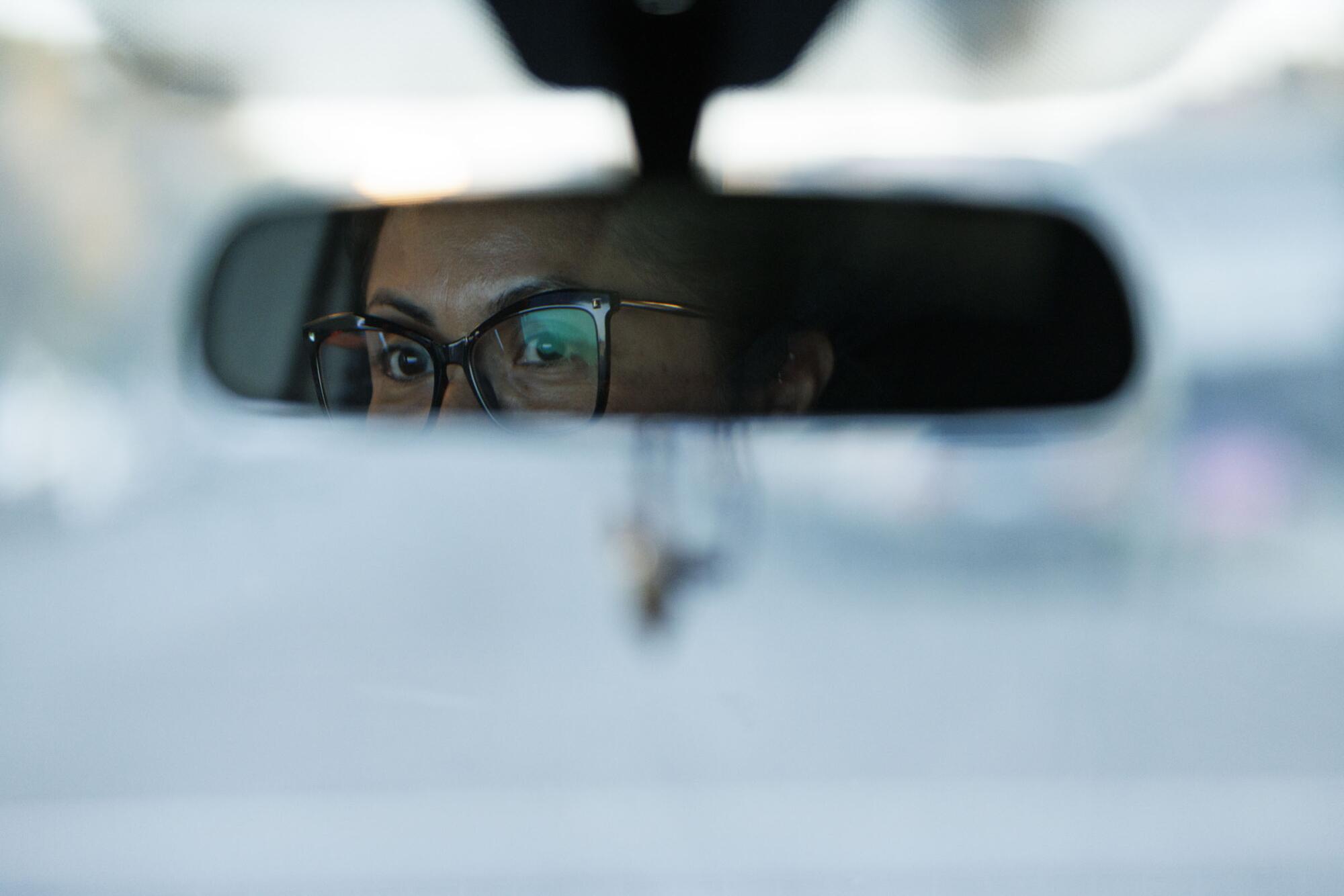 A woman with glasses is seen in a car mirror.