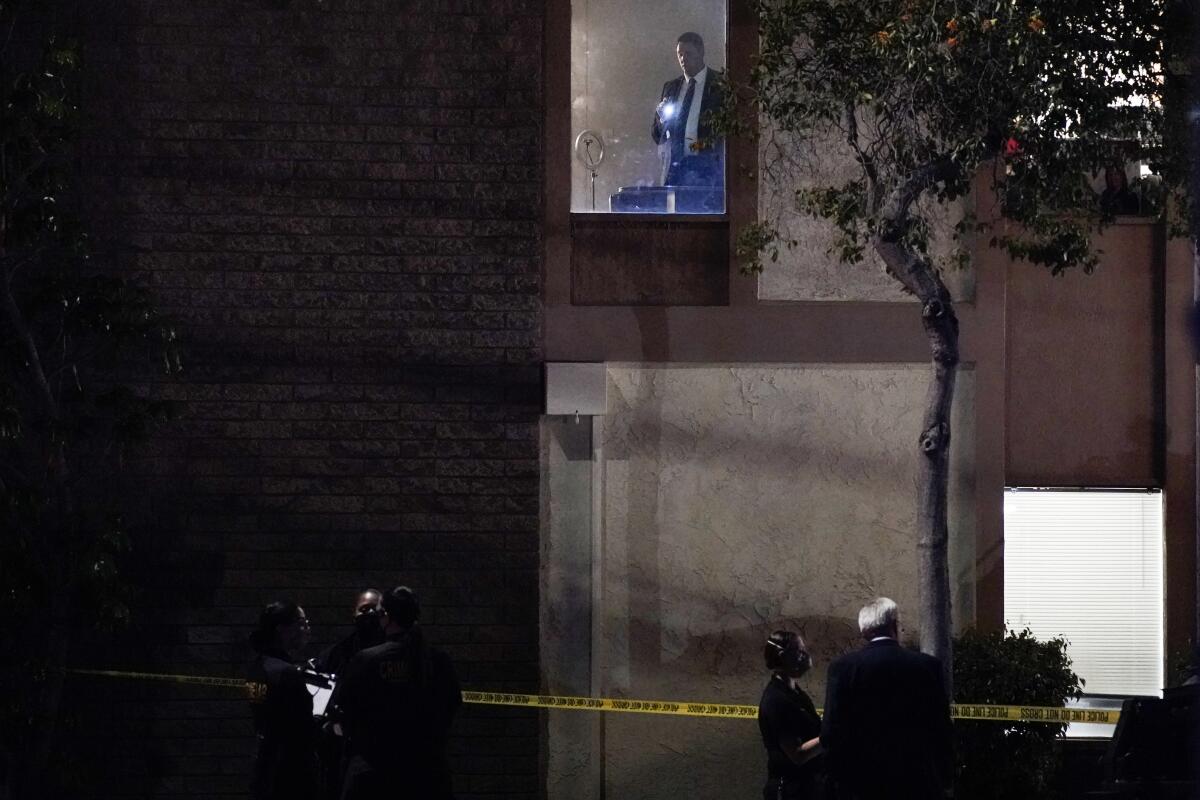Police stand outside yellow crime scene tape around a building as a man with a flashlight is seen in a second-story window