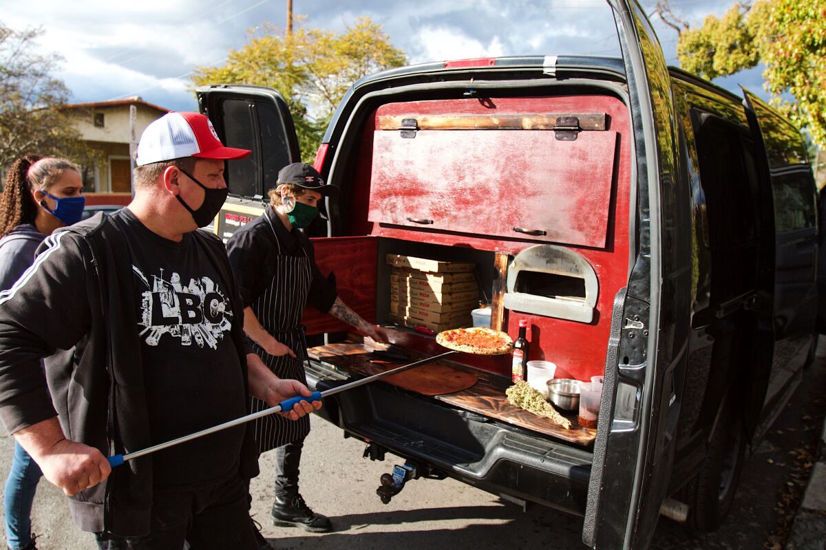 A man uses a peel to put a pizza into an oven in the back of a van. 