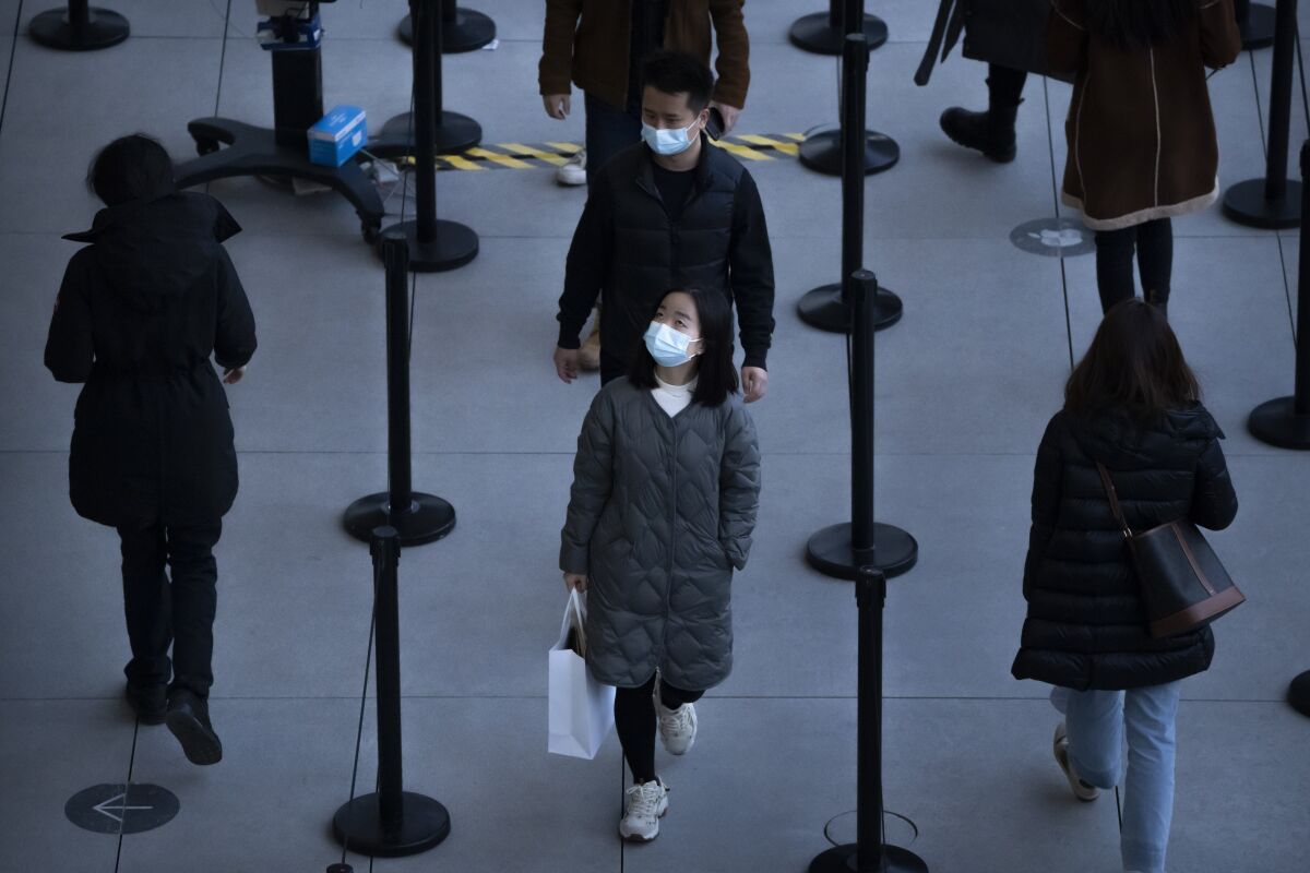 People wearing face masks to protect against COVID-19 wait in line to enter a store at an outdoor shopping center in Beijing, Saturday, Nov. 13, 2021. (AP Photo/Mark Schiefelbein)
