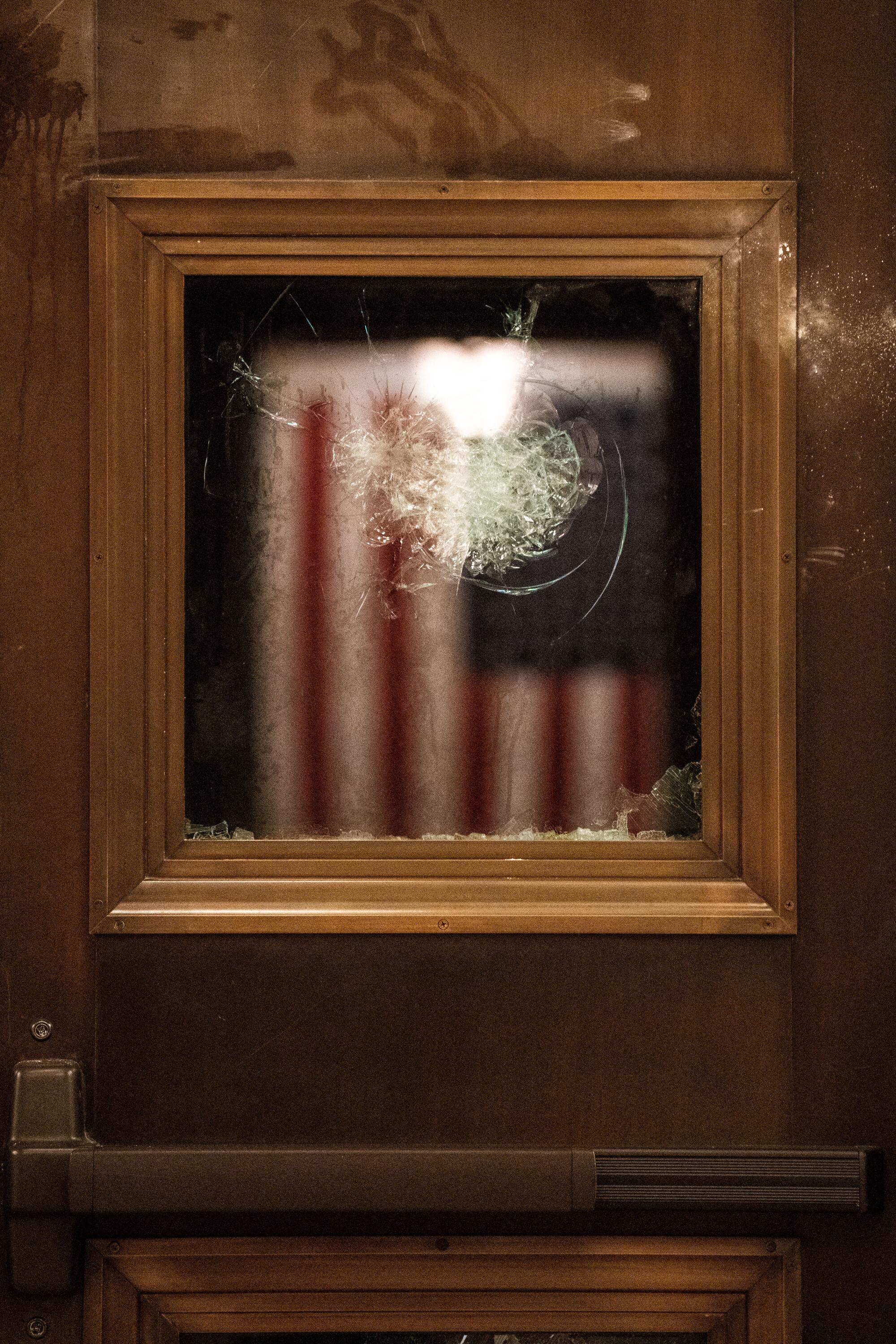 A blurred U.S flag hangs behind a broken window 