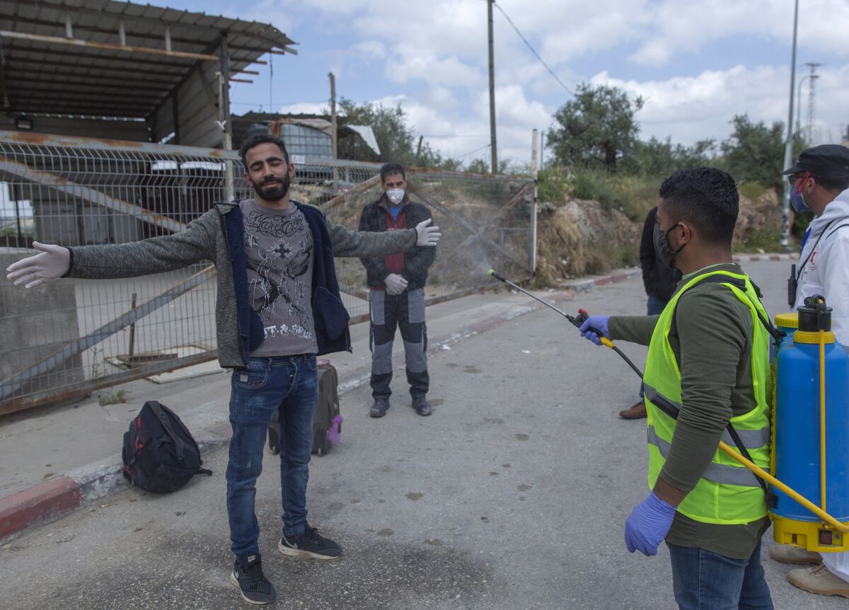 A paramedic sprays disinfectant on Palestinian laborers as they exit an Israeli army checkpoint April 7 near the West Bank village of Nilin.