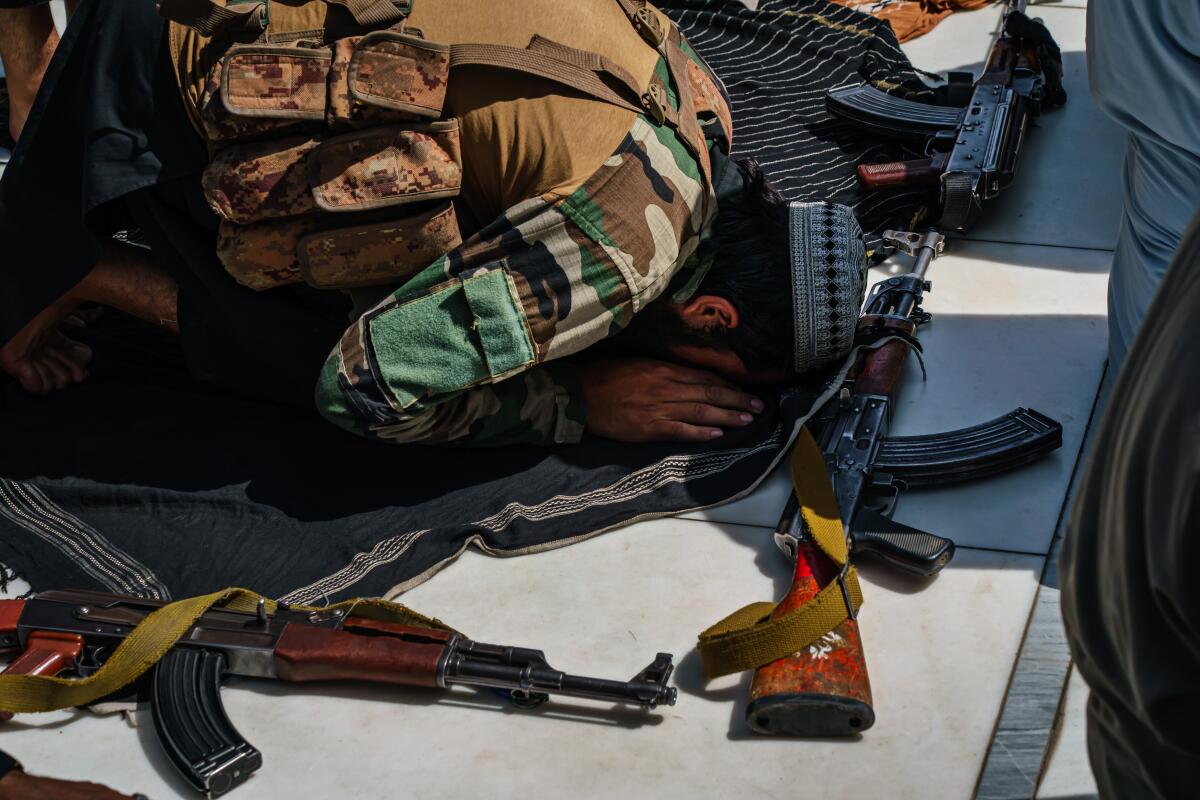 A member of the Taliban bows his head to the floor next to his weapon