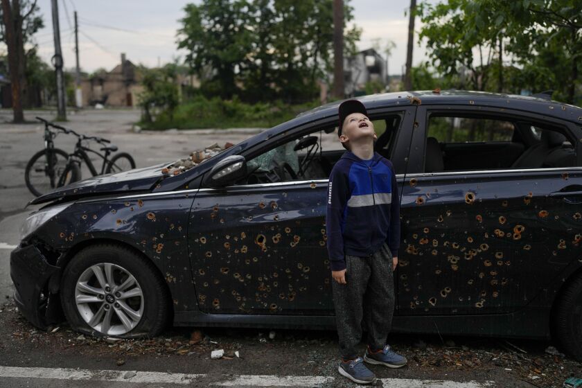 A child standing next to a damaged car looks up at a building destroyed during attacks in Irpin, on the outskirts Kyiv, Ukraine, Monday, May 30, 2022. (AP Photo/Natacha Pisarenko)