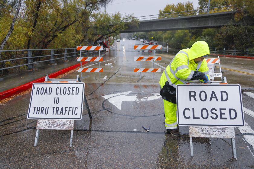 Miles Tufaga sets up road closed signs on Ward Road at Camino Del Rio North in Mission Valley to prevent vehicles from driving over the San Diego River that had already started flooding the roadway before 2 p.m., November 28, 2019, in San Diego, California.