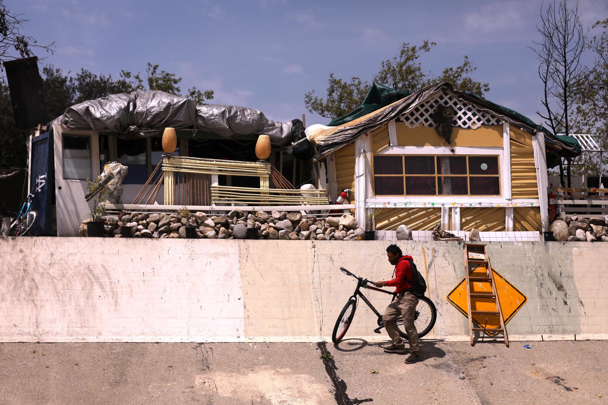 A man with a bicycle next to his makeshift home above a flood channel