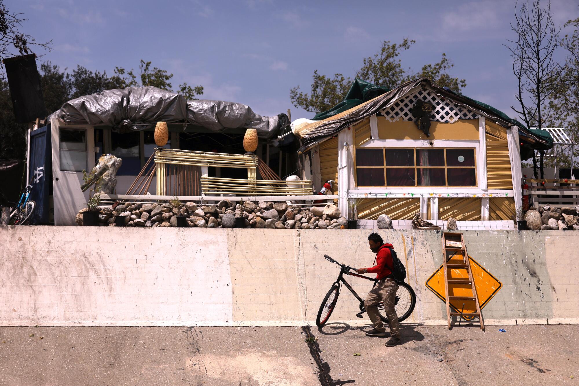 A man with a bicycle next to his makeshift home above a flood channel 