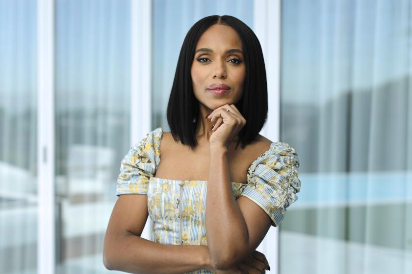 Kerry Washington stands in a room with her hand on her chin. 