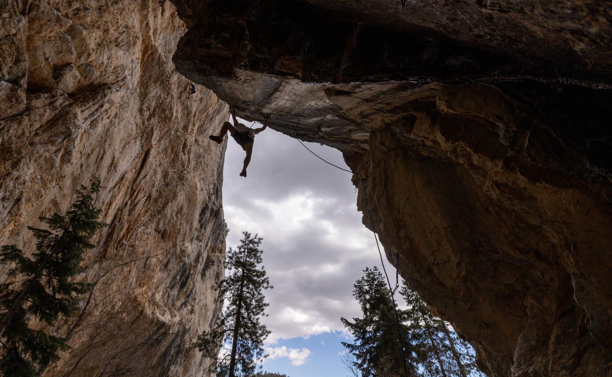  A climber hangs high off the ground from a horizontal shelf of rock.  