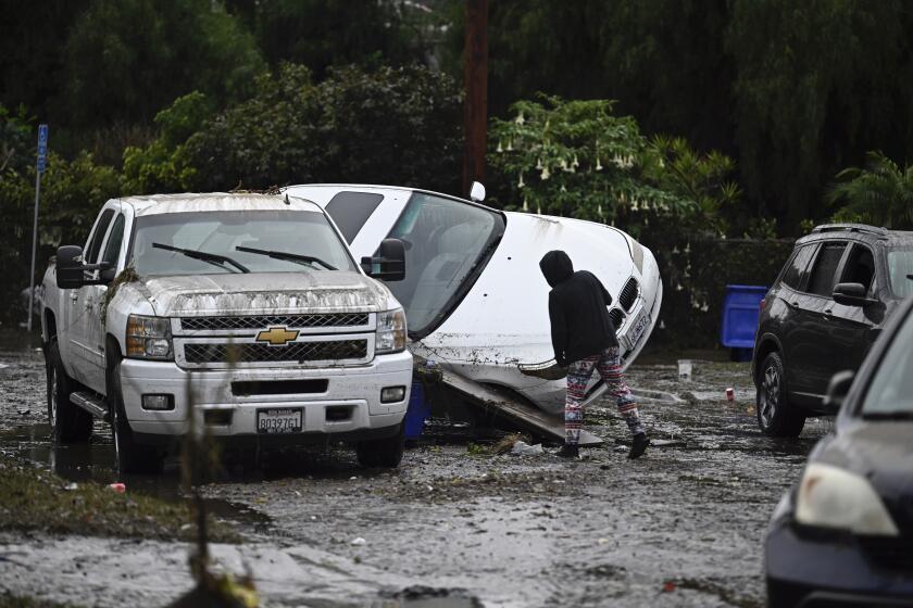 A woman examines cars damaged from floods during a rain storm Monday, Jan. 22, 2024, in San Diego. (AP Photo/Denis Poroy)
