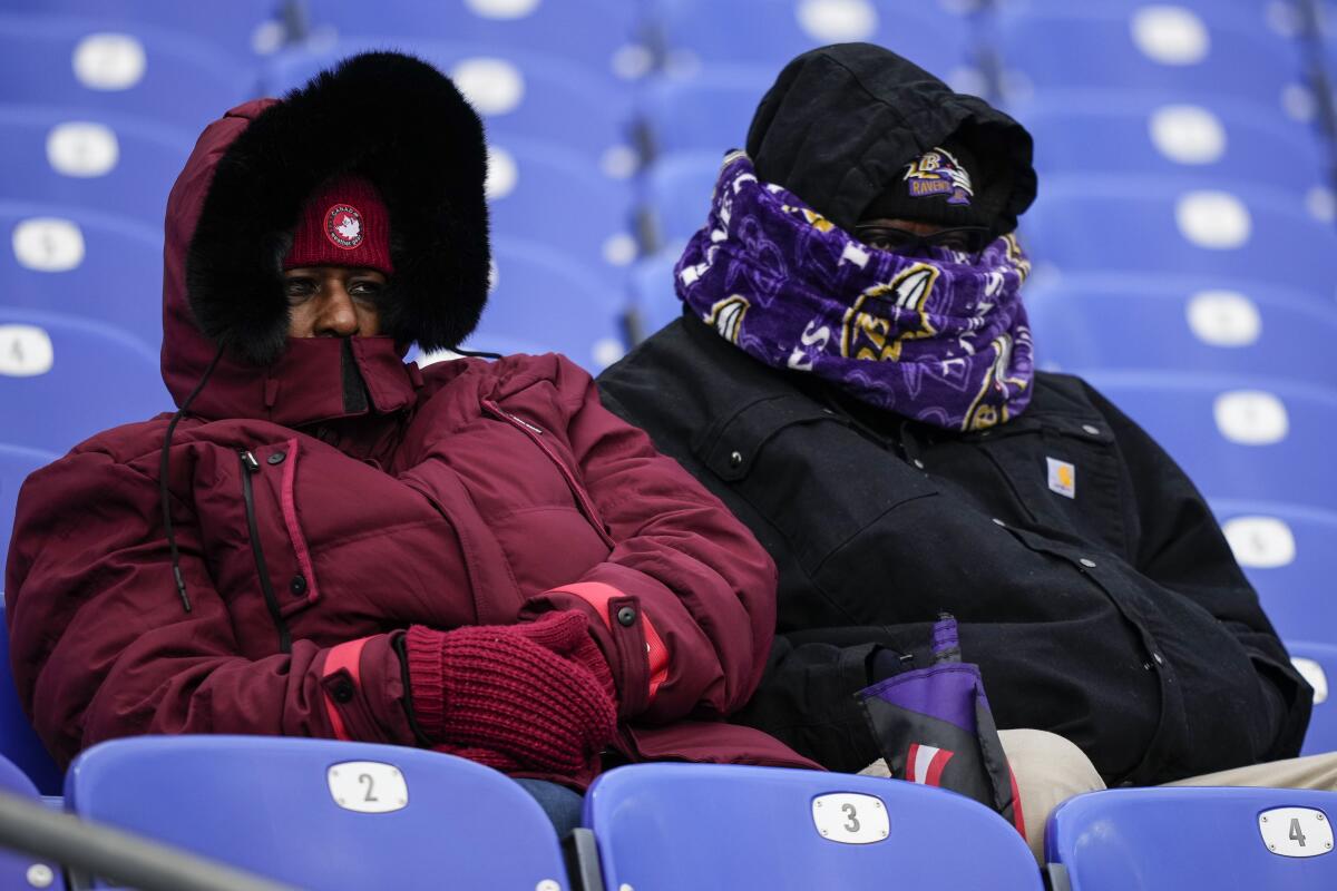 Dos personas de cobijan del frío en el partido de fútbol americano entre los Ravens de Baltimore