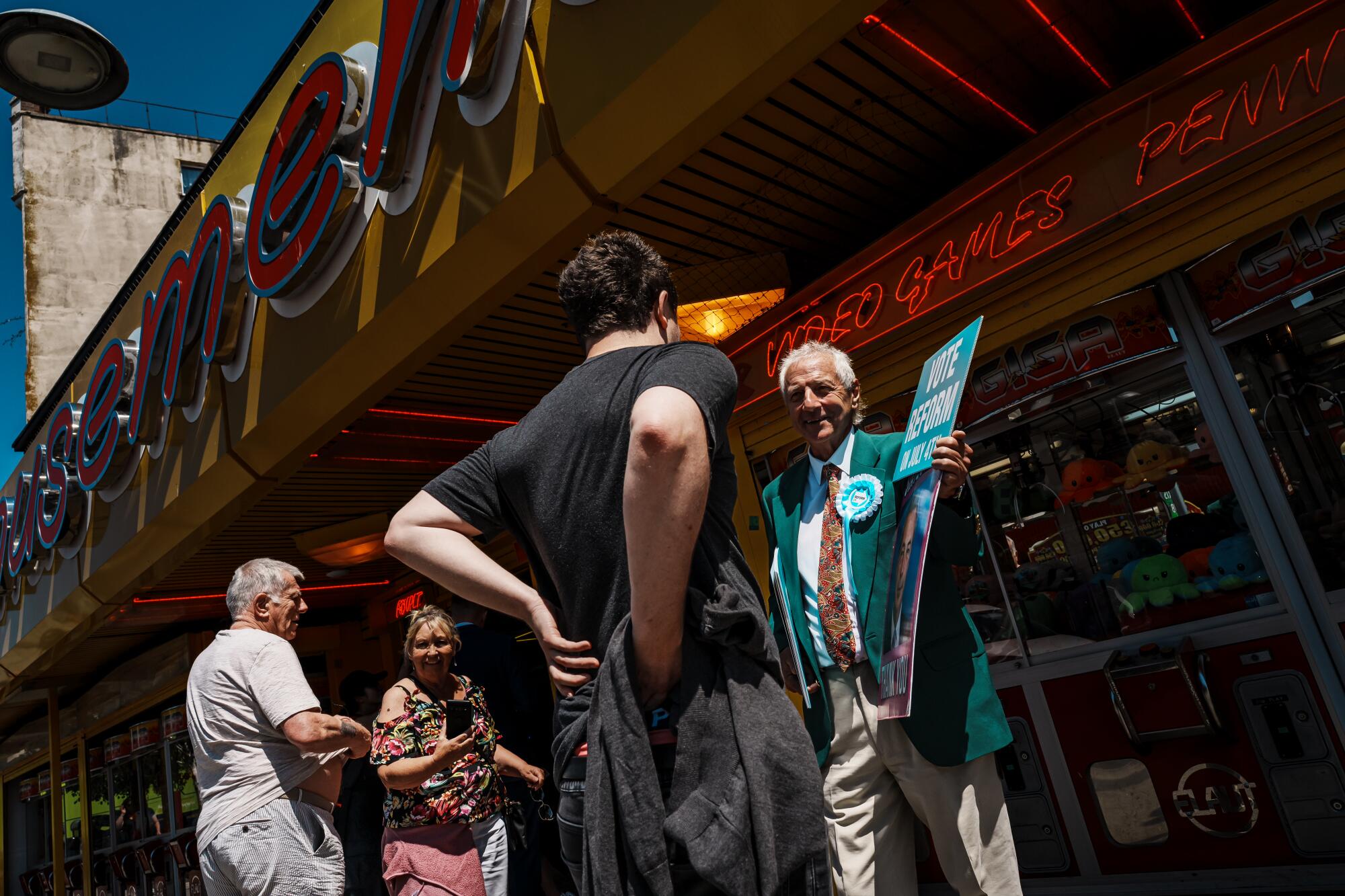 A man in a green jacket campaigns for Nigel Farage outside an arcade. 