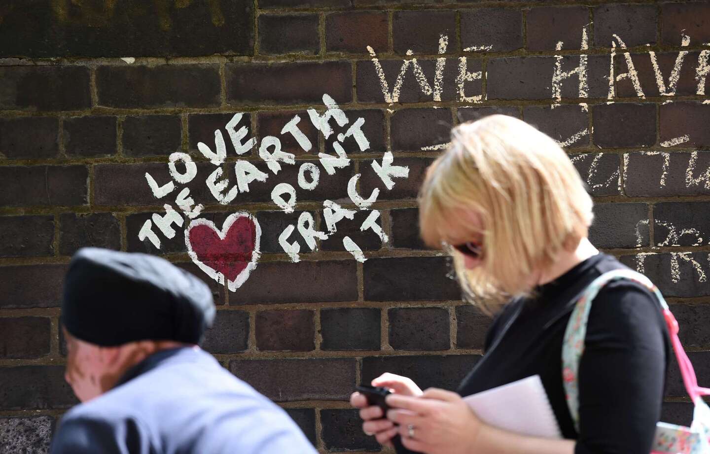 People walk past anti-fracking messages written on a wall during a demonstration outside Lancashire County Hall in northwest England, against the applications from energy firm Cuadrilla to start two fracking operations on nearby sites.