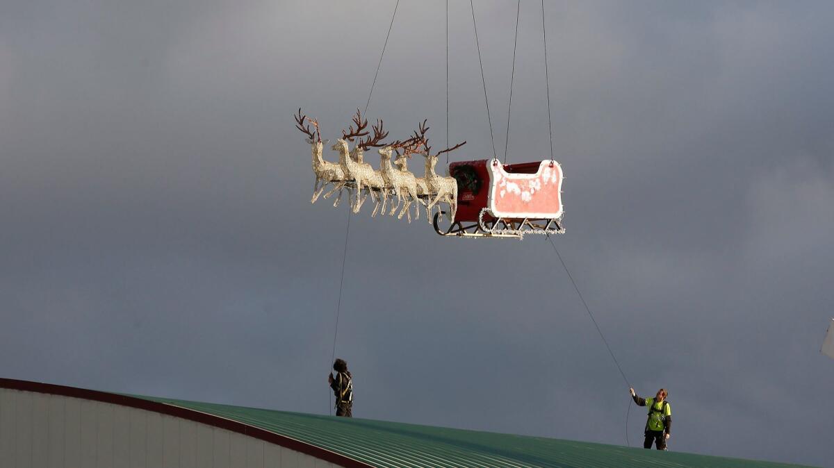 Santa's sleigh and reindeer are carefully guided into position from a crane by two workers on the roof of the Hangar as workers prepare for Winter Fest at the OC Fair & Event Center on Thursday evening.