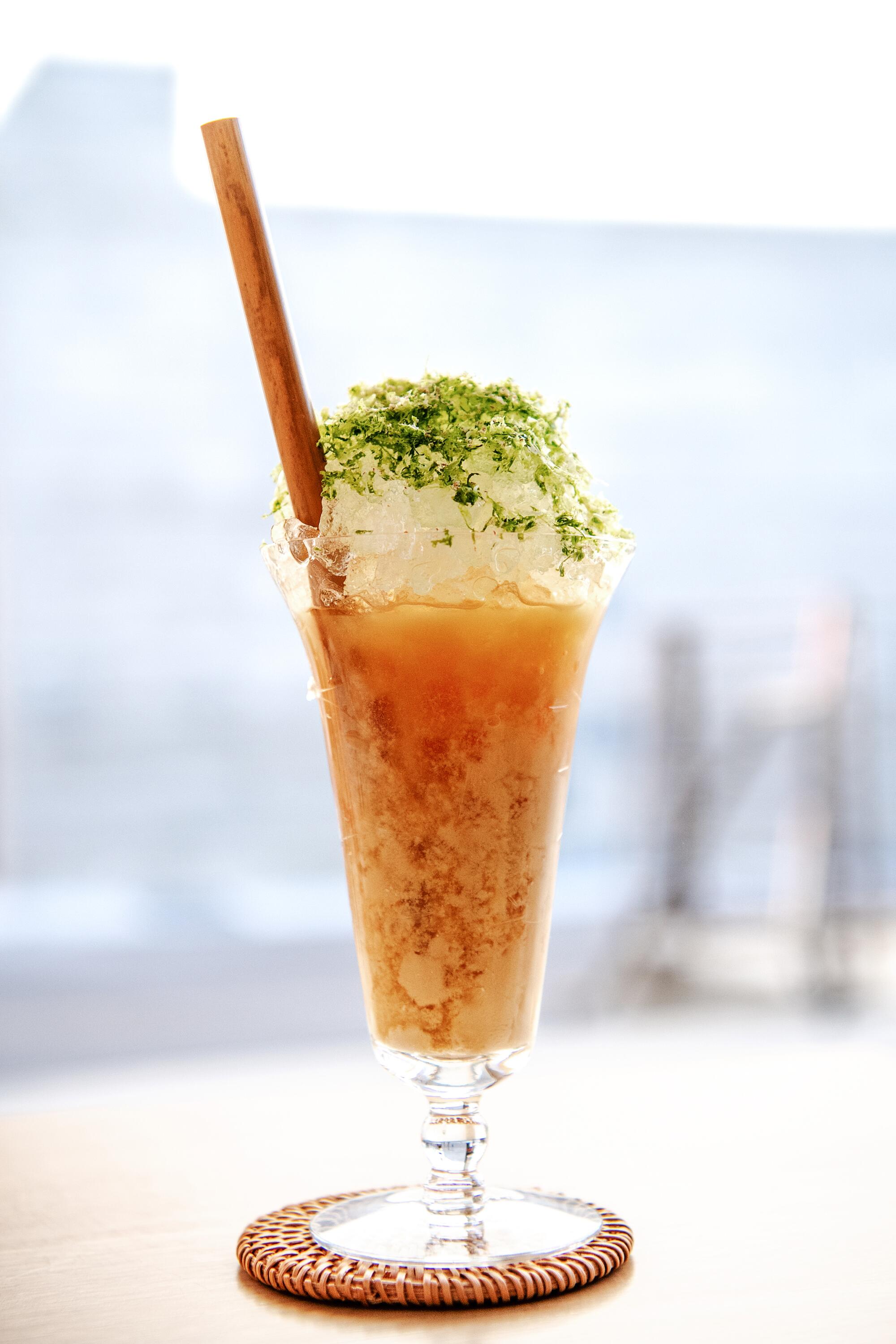 An iced cocktail in a tall glass with a wooden straw and garnish at Kato.