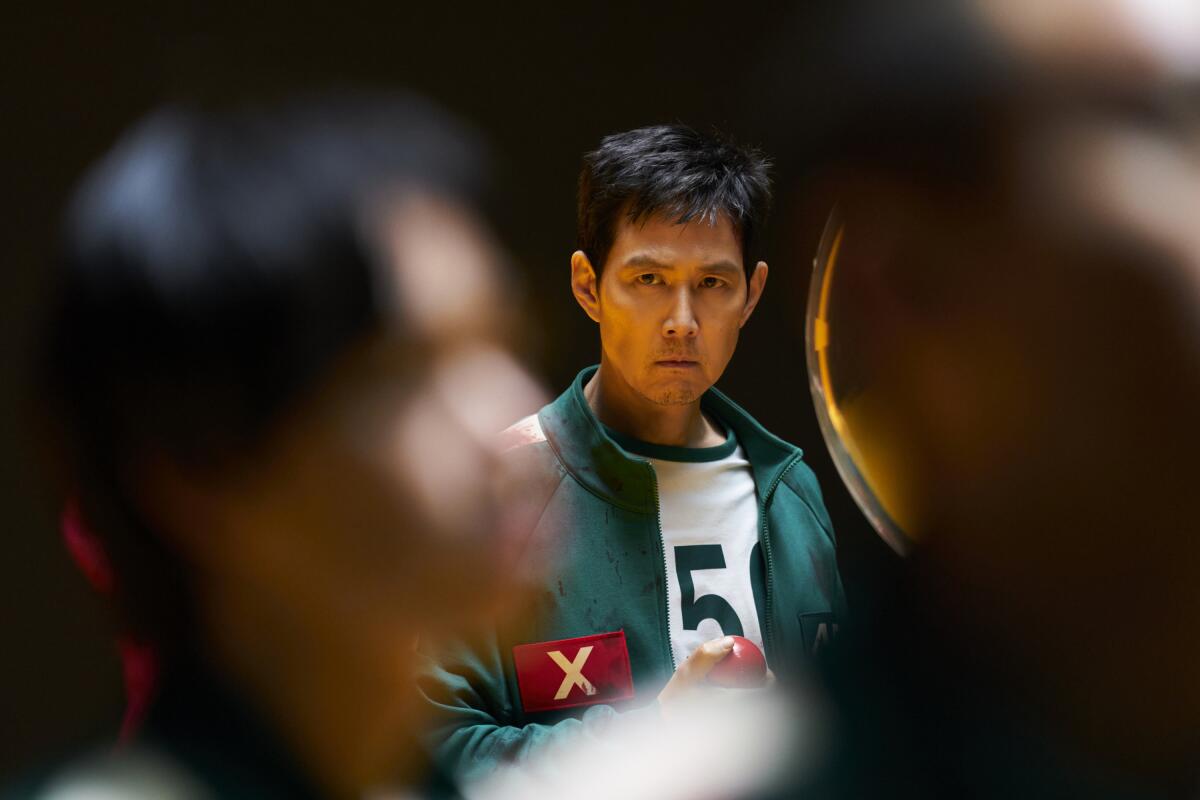 A man in a green track suit seen from afar with a blurry pair of people in front of him.