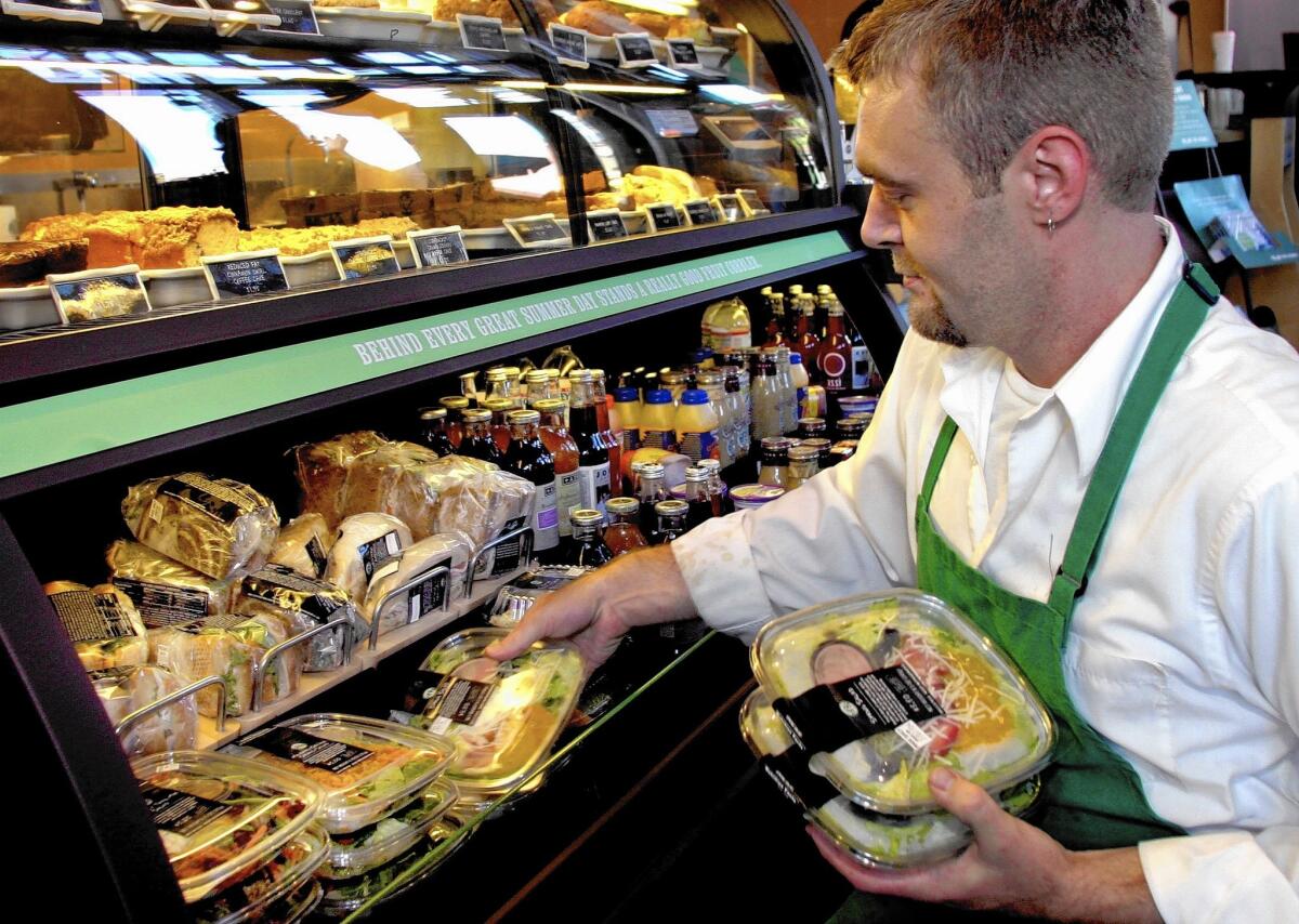 Adam Greener stocks a refrigerated case of sandwiches, salads and cold drinks at a Starbucks store in Denver in 2004. The company has announced that it intends to donate all its leftover food to charity.