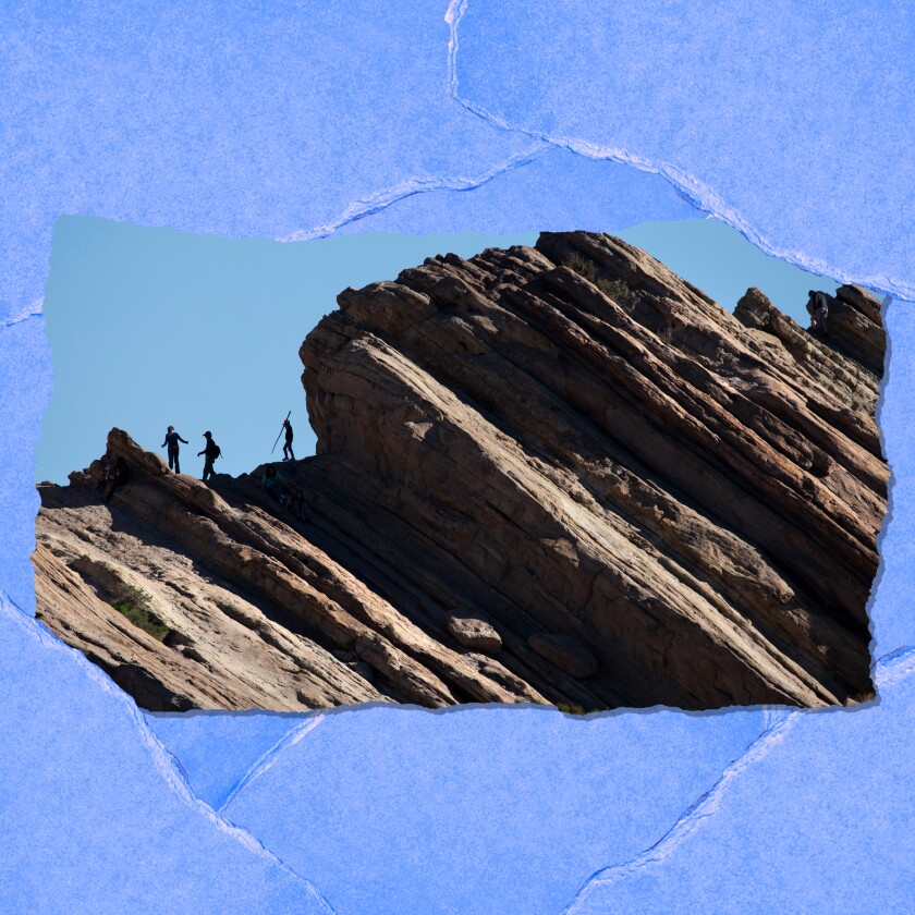 Several people are seen from a distance climbing on a large rock formation.