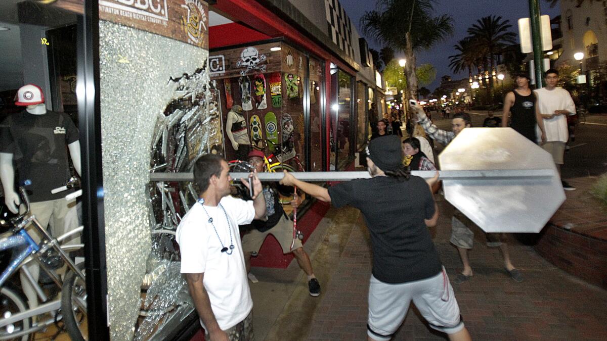 A rioter pushes a stop sign through a window of the retailer Easyrider, at Main and Orange streets in downtown Huntington Beach, following the U.S. Open of Surfing contest finals July 28, 2013.