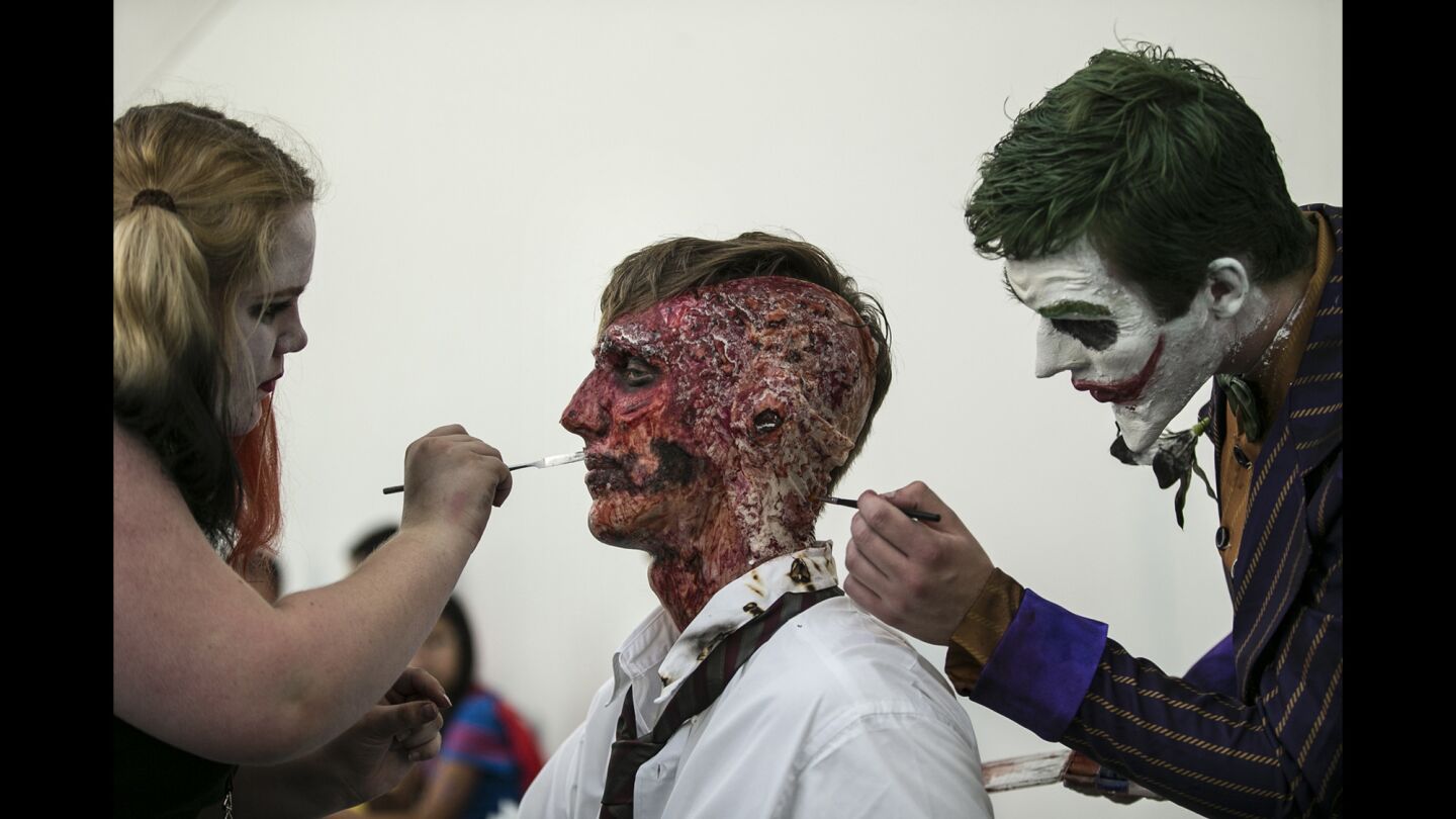 Amanda McGowan as Harley Quinn, left, and PJ Williamson as the Joker, right, apply makeup to Tyler Kluska as Two-Face halfway through a long day of cosplay at Comic-Con 2016.