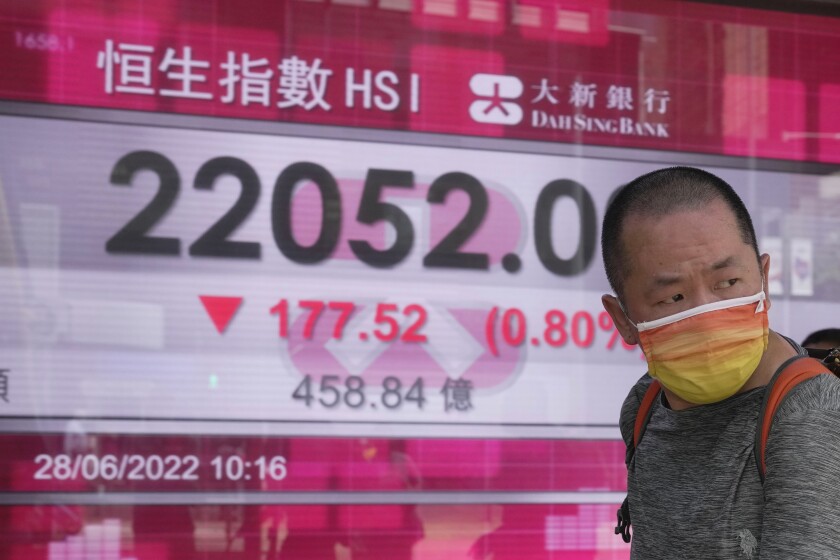 A man wearing a face mask walks past a bank's electronic board showing the Hong Kong share index in Hong Kong, Tuesday, June 28, 2022. Asian shares were mixed Tuesday after a wobbly day on Wall Street as markets cooled off following a rare winning week.(AP Photo/Kin Cheung)